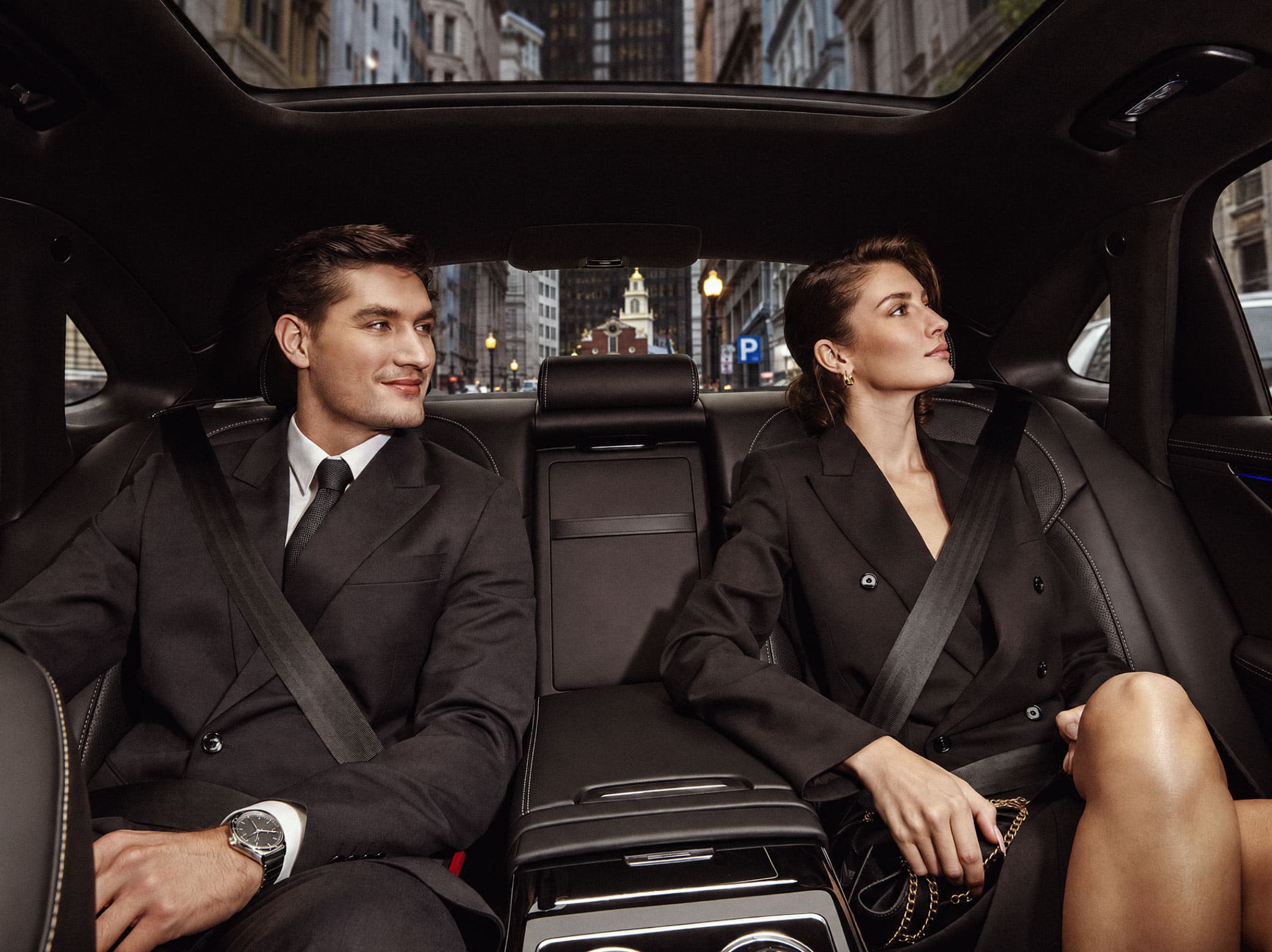 Two passengers in the back seat of a luxury sedan looking out at the city